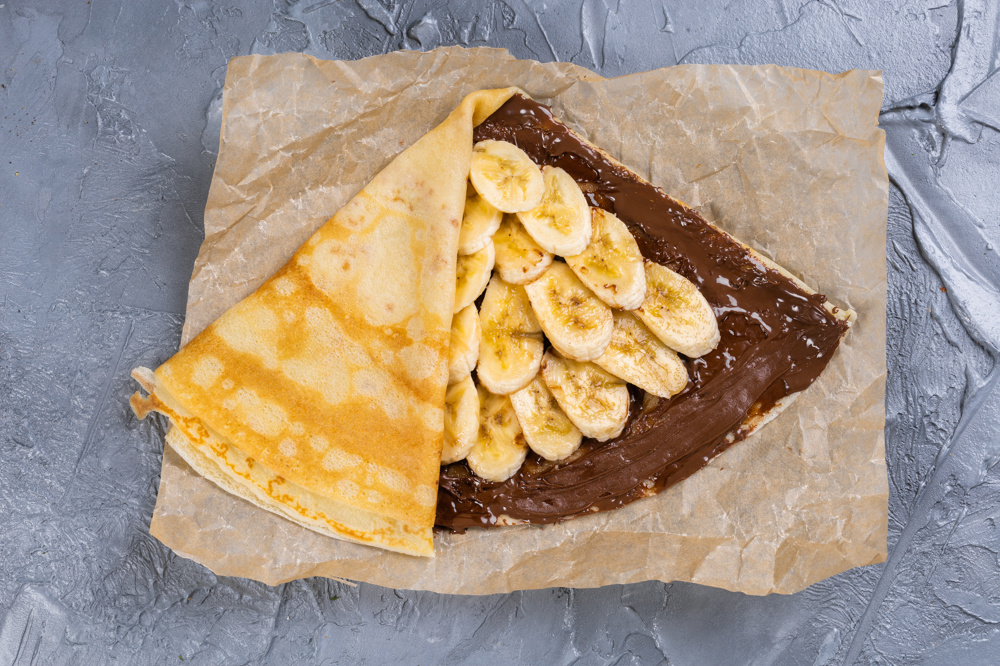 Yağlı kağıdın üzerinde bir krep, çikolata kreması ve muzlar üzerinde.