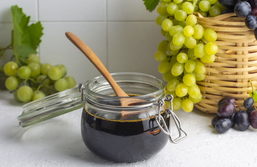 1 Kase pekmez, arkada yeşil üzümler görünüyor.