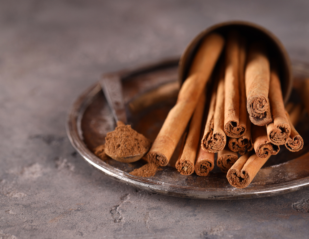 Bir tatlı kaçığı toz tarçın yanında birkaç adet çubuk tarçın.
